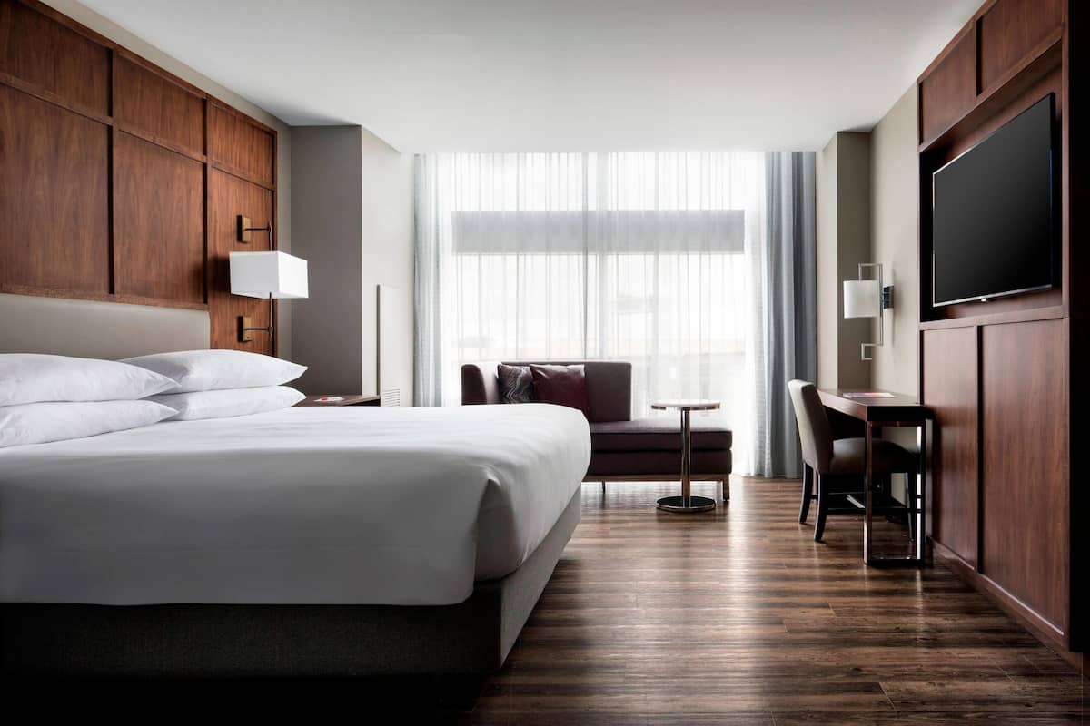 Habitación de hotel con una cama grande, un escritorio, una silla, un televisor y una ventana con cortinas.
