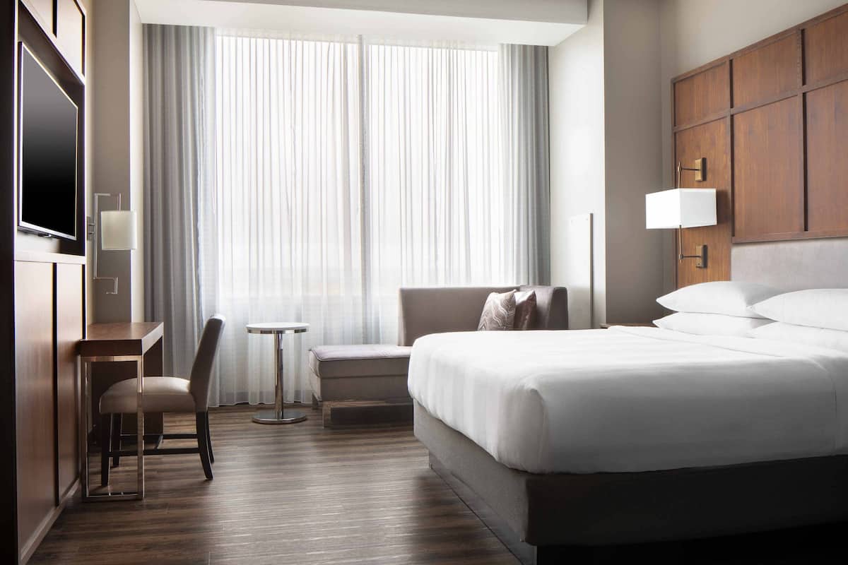 Una habitación de hotel con una cama grande, un escritorio, una silla, una mesita pequeña y un televisor.