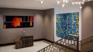 A modern lobby with a reception desk, a staircase, and two large abstract art pieces on the walls.