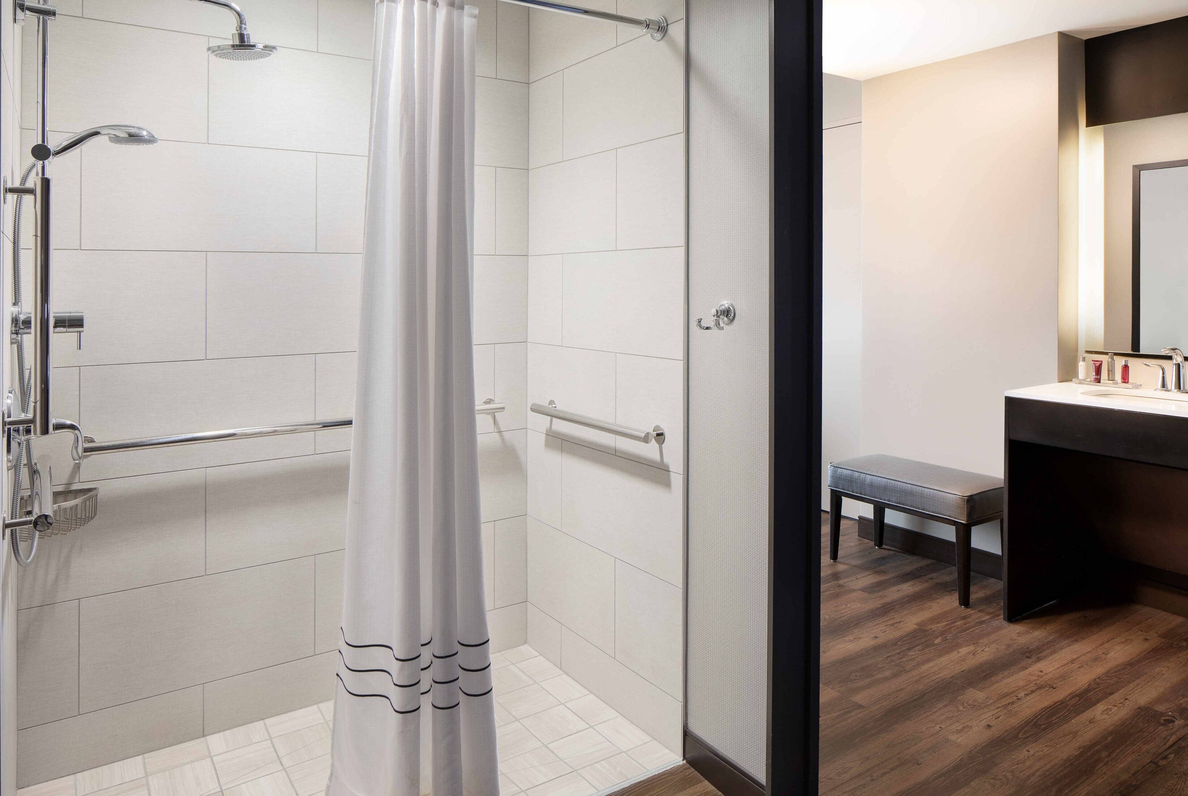 Un baño moderno con ducha, un banco y tocador con espejo.