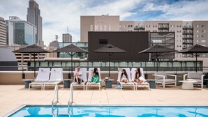 Un espace piscine sur le toit, avec des chaises longues et des parasols, offrant une vue dégagée sur les gratte-ciel de la ville, et un bâtiment portant l’inscription « OMAHA ».