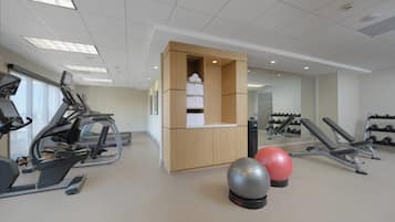 Une salle de sport équipée de matériel d’exercice, un meuble en bois contenant des serviettes et un miroir.