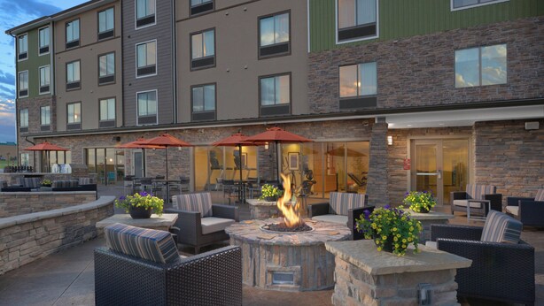An outdoor patio with stone seating, a fire pit, and umbrellas. - TownePlace Suites by Marriott Denver South/Lone Tree (Lone Tree)