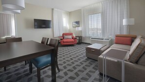 A hotel room with a dining table, a sofa, a red armchair, a TV mounted on the wall, and a window with curtains. - TownePlace Suites by Marriott Denver South/Lone Tree (Lone Tree)