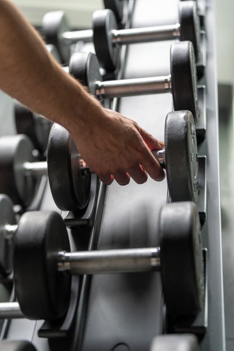 A hand adjusting a weight on a rack of dumbbells.