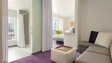Habitación de hotel con cama, sofá, una mesita y vista a la ciudad desde la ventana.