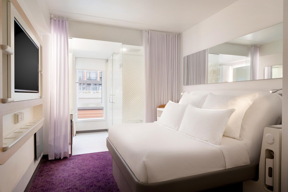 A hotel room with a bed, a TV, a bathroom, and a view of the outside.