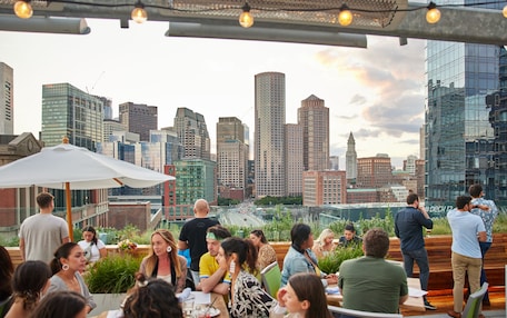 A rooftop bar with a city skyline view, outdoor seating, and string lights.