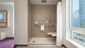 A modern bathroom with a shower, a toilet, and a sink. There is a window with a view of a building outside. - YOTEL Boston, Select by Hilton (Boston)