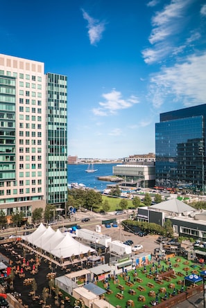 A cityscape with modern buildings, a waterfront, and a green outdoor dining area with tents. - YOTEL Boston (Boston)