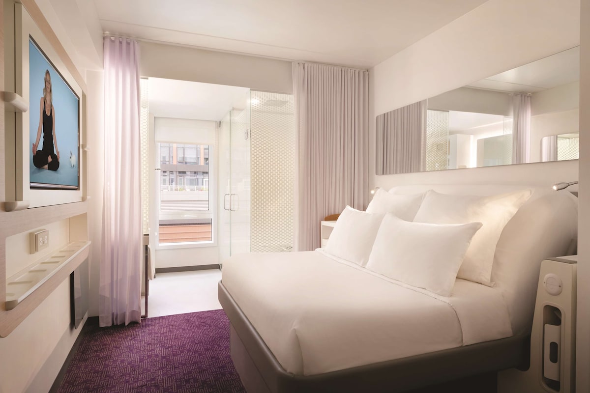 Ein Hotelzimmer mit Bett, Fernseher, Badezimmer und Blick ins Freie.