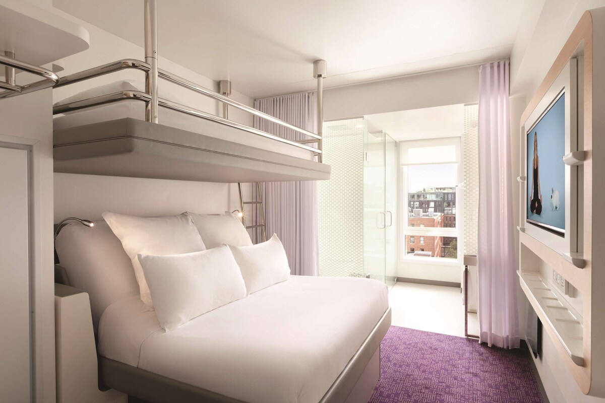 Ein modernes Hotelzimmer mit Bett, Fernseher und einem Balkon mit Vorhängen.