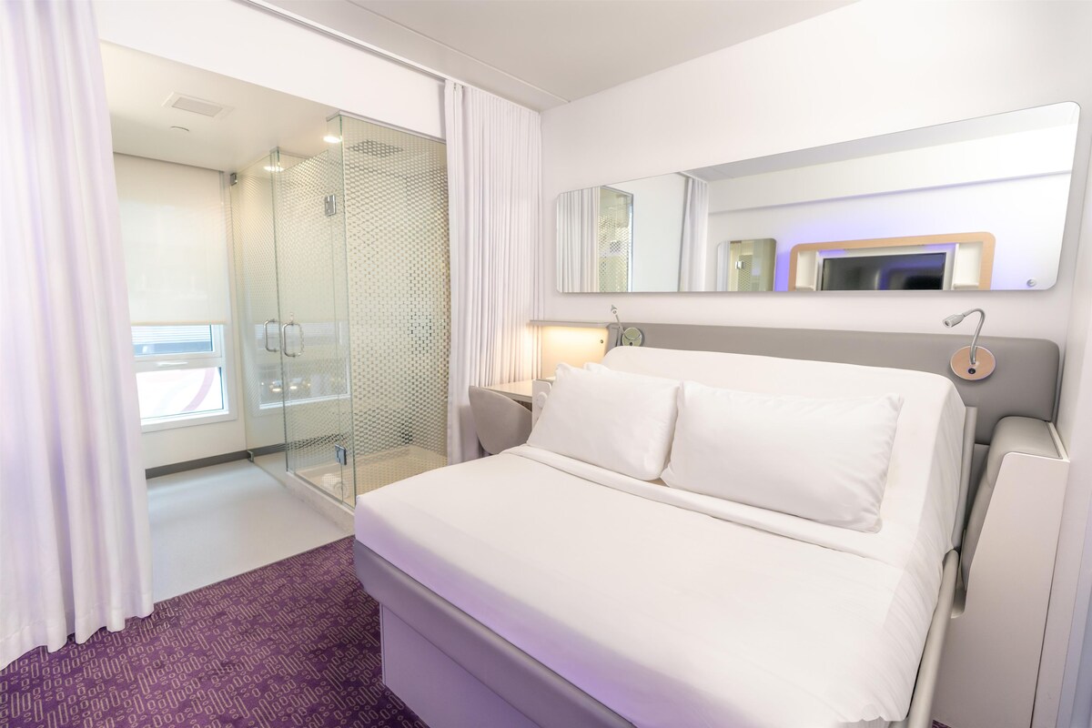 Una habitación de hotel con cama, ducha, espejo y mesita de noche.