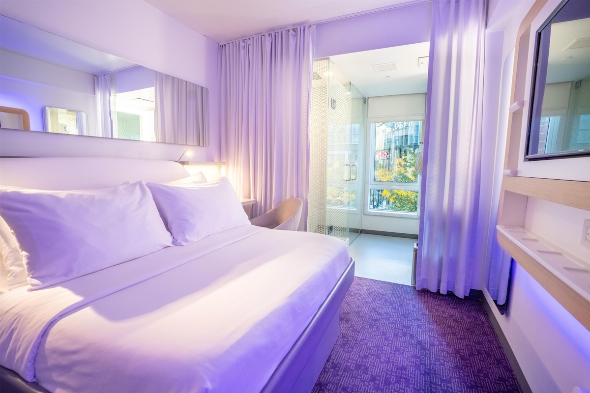 A hotel room with a bed, a desk, a chair, a window, and a door leading to a balcony.