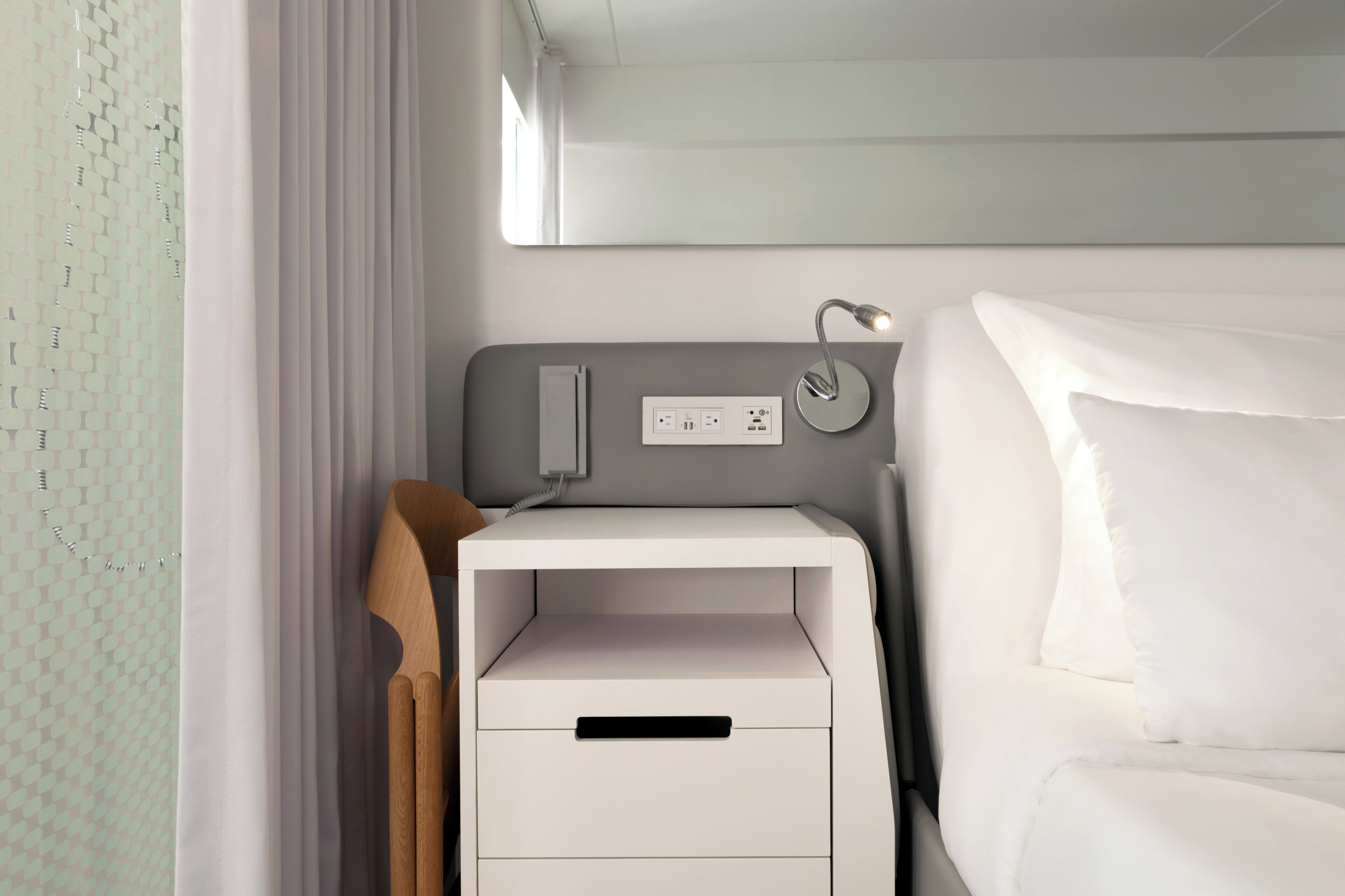 A modern hotel room with a bed, a bedside table with a lamp, and a power outlet.