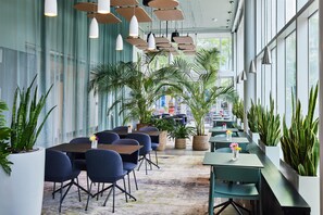 A modern indoor dining area with tables and chairs, large windows, and hanging pendant lights. - YOTEL Boston, Select by Hilton (Boston)