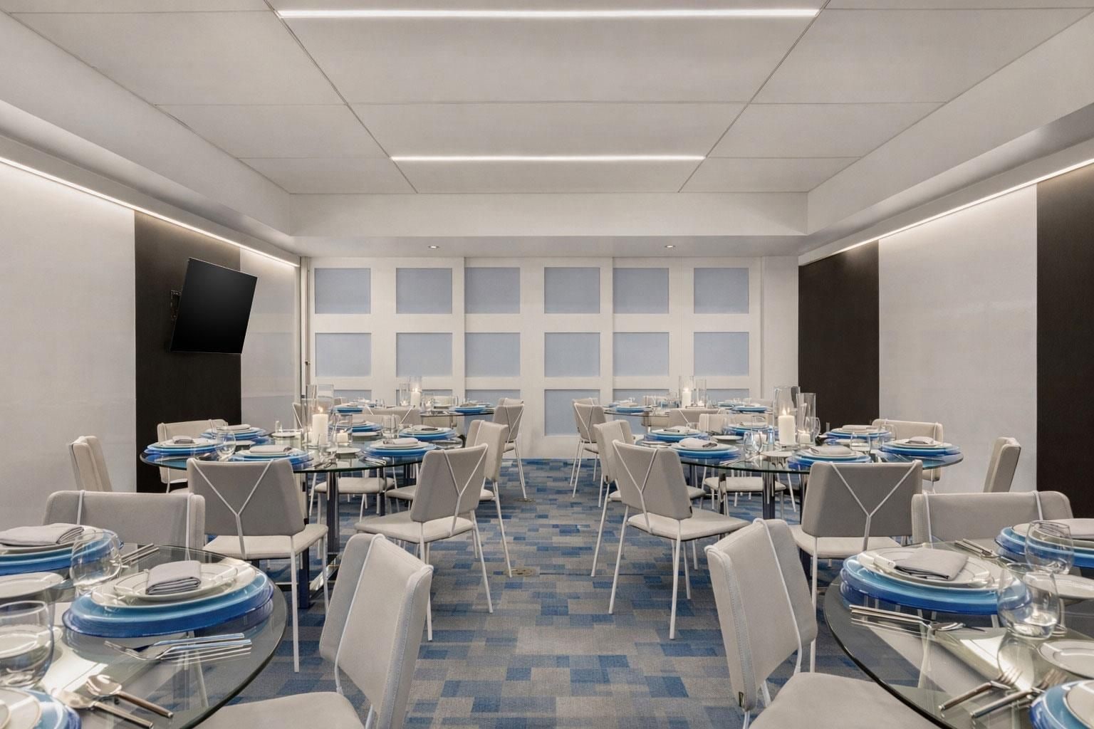 Una sala conferenze con diversi tavoli apparecchiati per la cena, completa di sedie e stoviglie.
