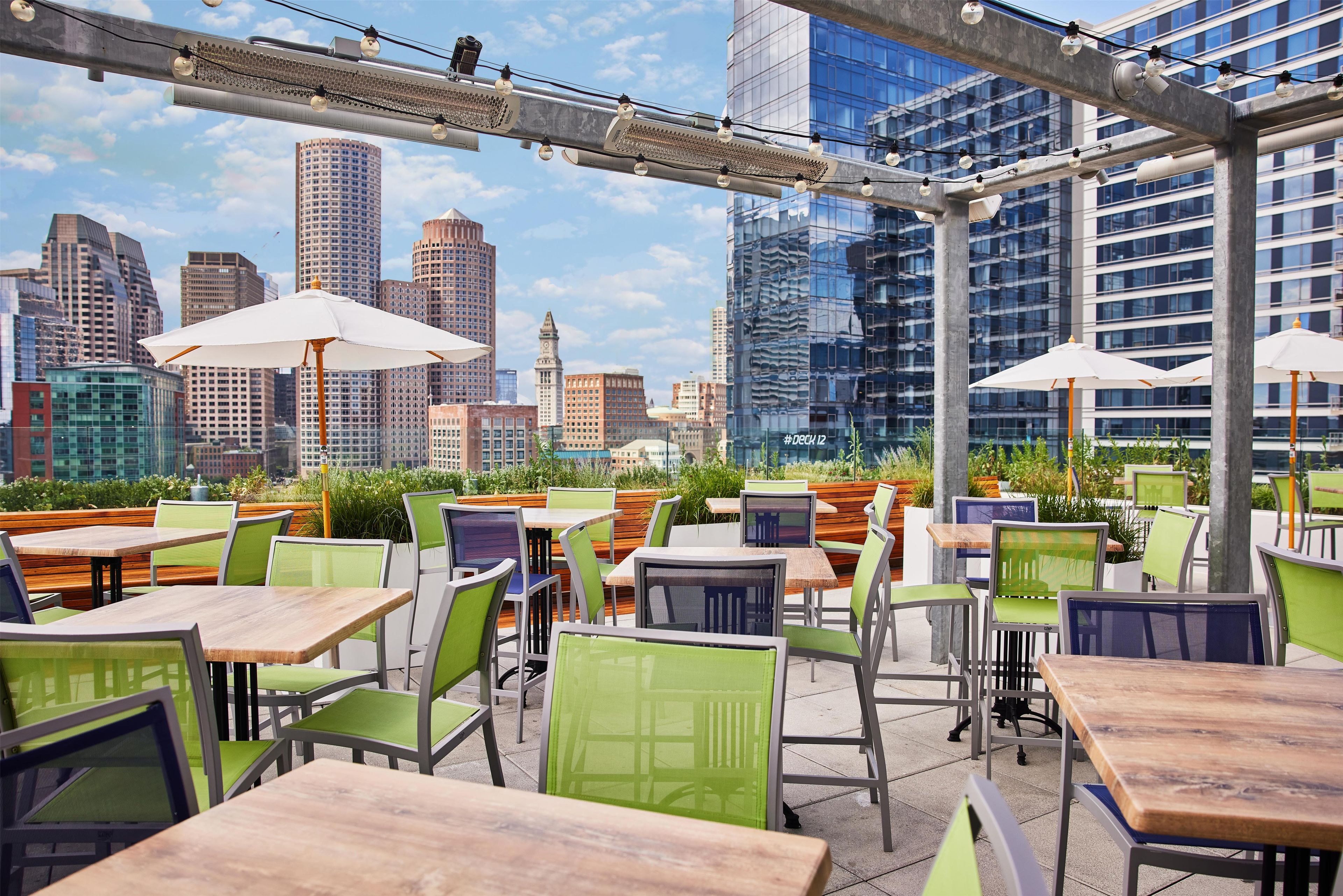 An outdoor seating area with tables and chairs, umbrellas, and a city skyline view.