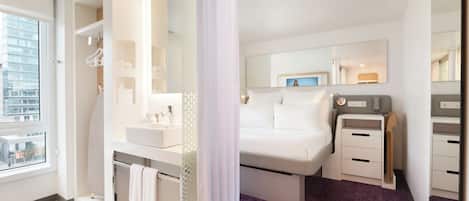 A modern hotel room with a large bed, a separate bathroom, and a view of the cityscape.