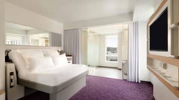Ein modernes Hotelzimmer mit einem großen Bett, einem Fernseher und Blick auf die Stadt durch das Fenster.