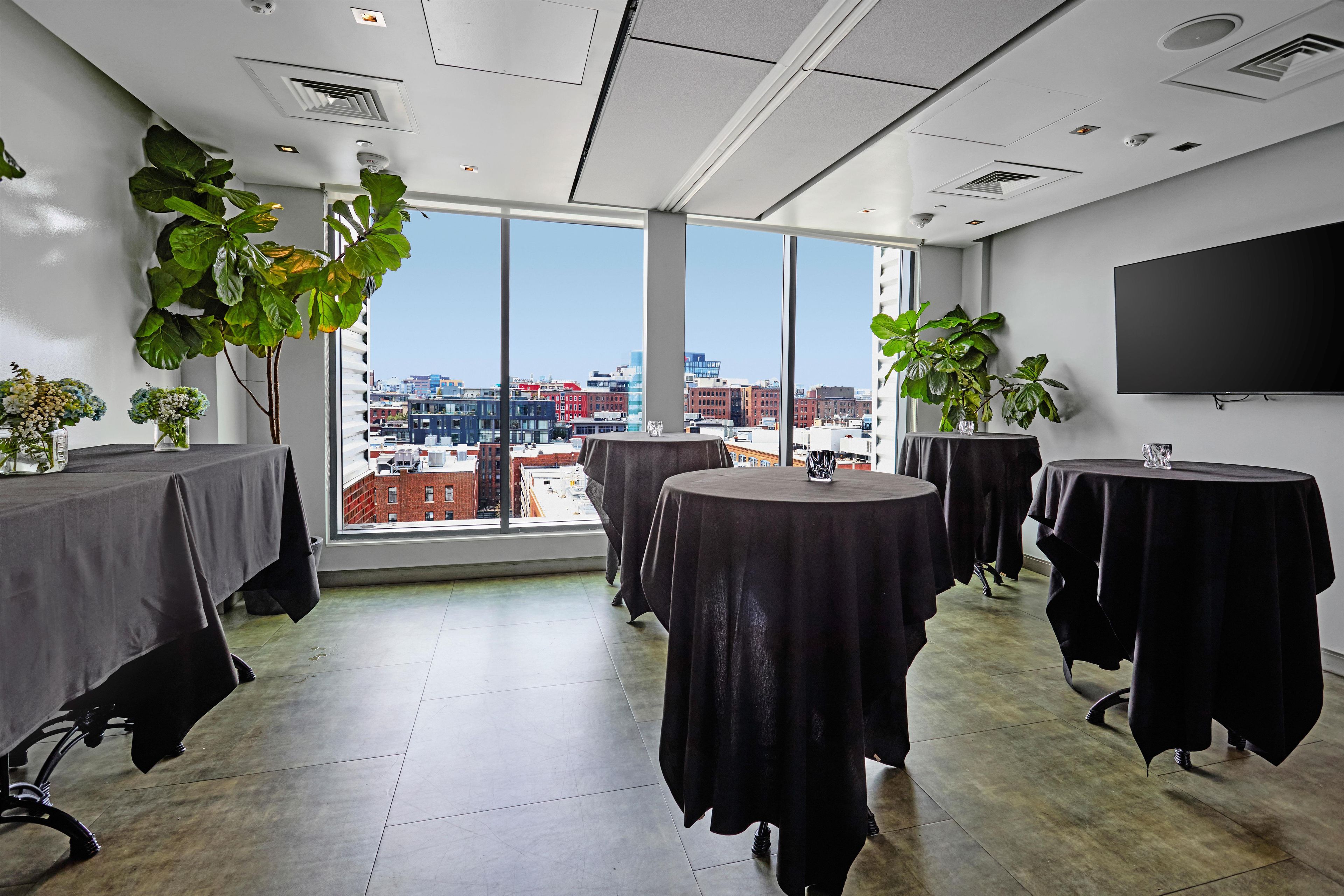 A conference room with large windows, multiple tables, and potted plants.