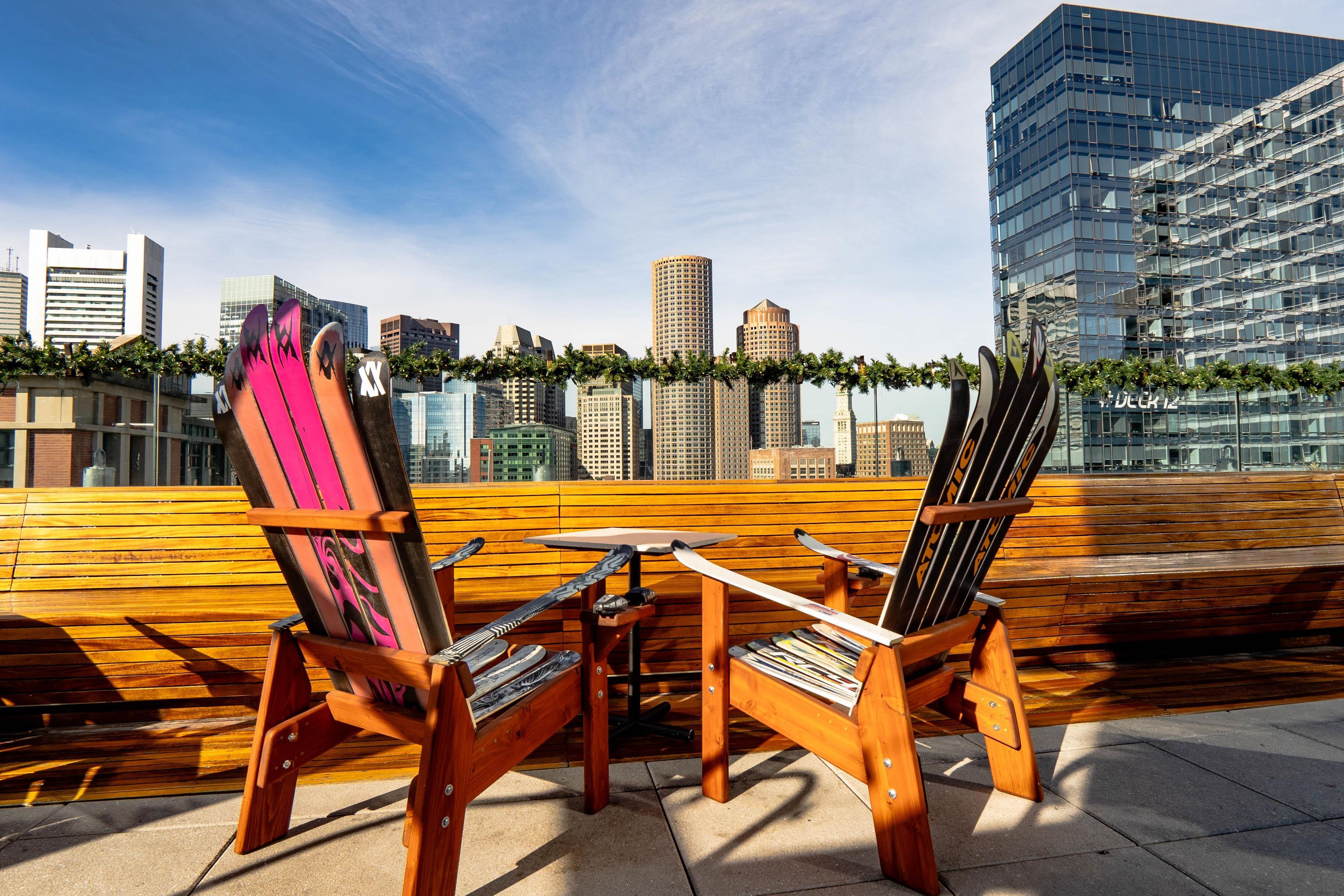 A rooftop terrace with two Adirondack chairs and a small table, overlooking a city skyline with modern buildings.