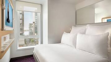 A hotel room with a bed, a window with a view of buildings, and a wall-mounted TV.