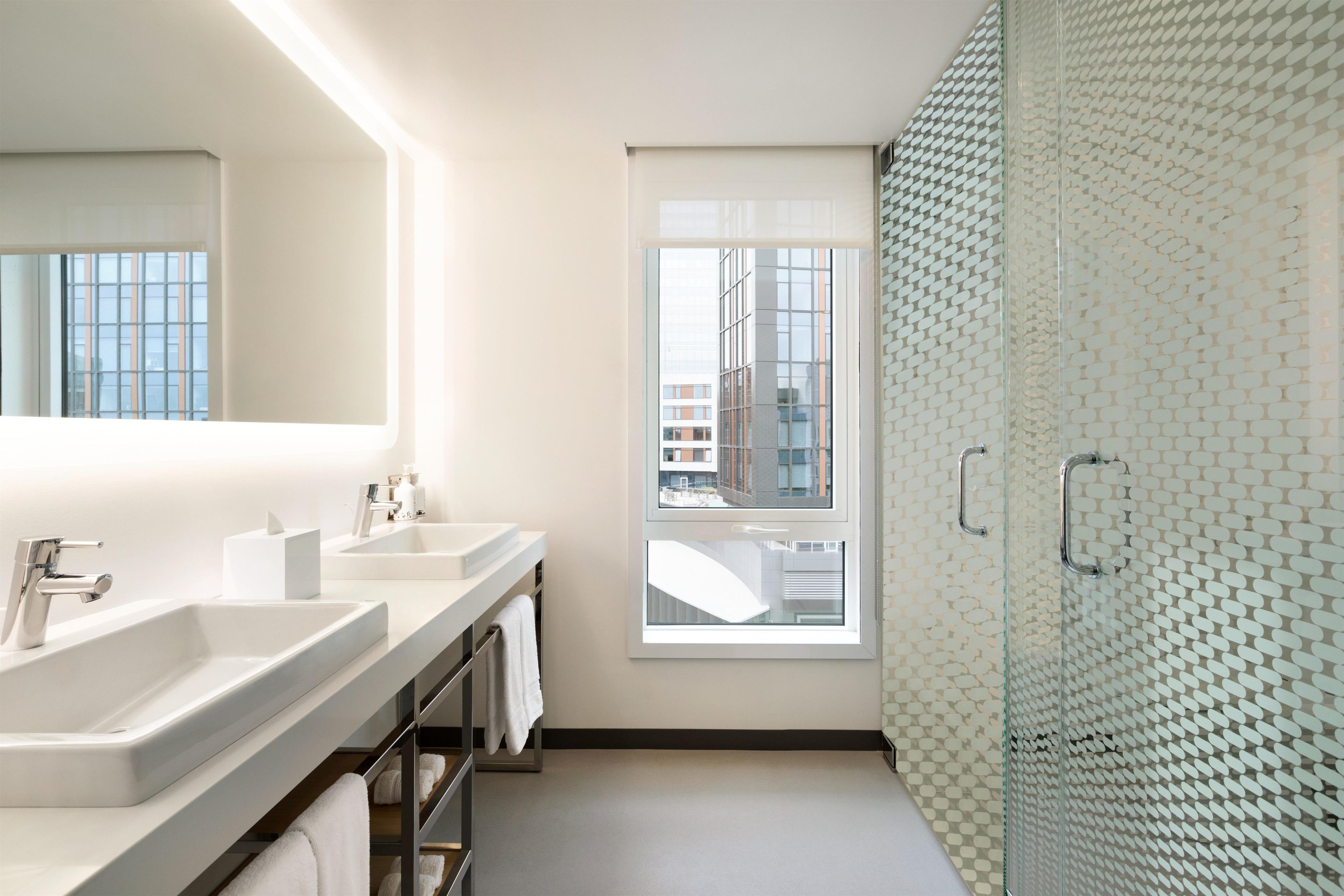 Une salle de bain moderne avec deux lavabos, un grand miroir et une douche à parois de verre.