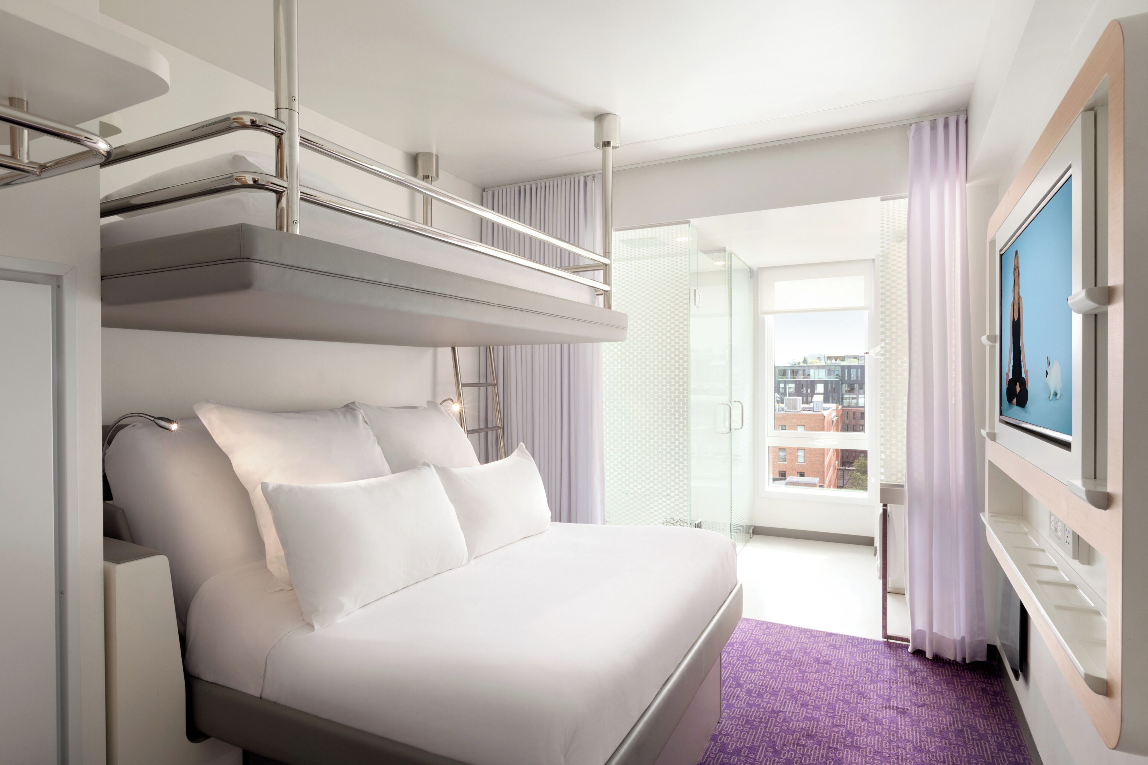 A hotel room with a bed, a TV, a balcony, and a city view.
