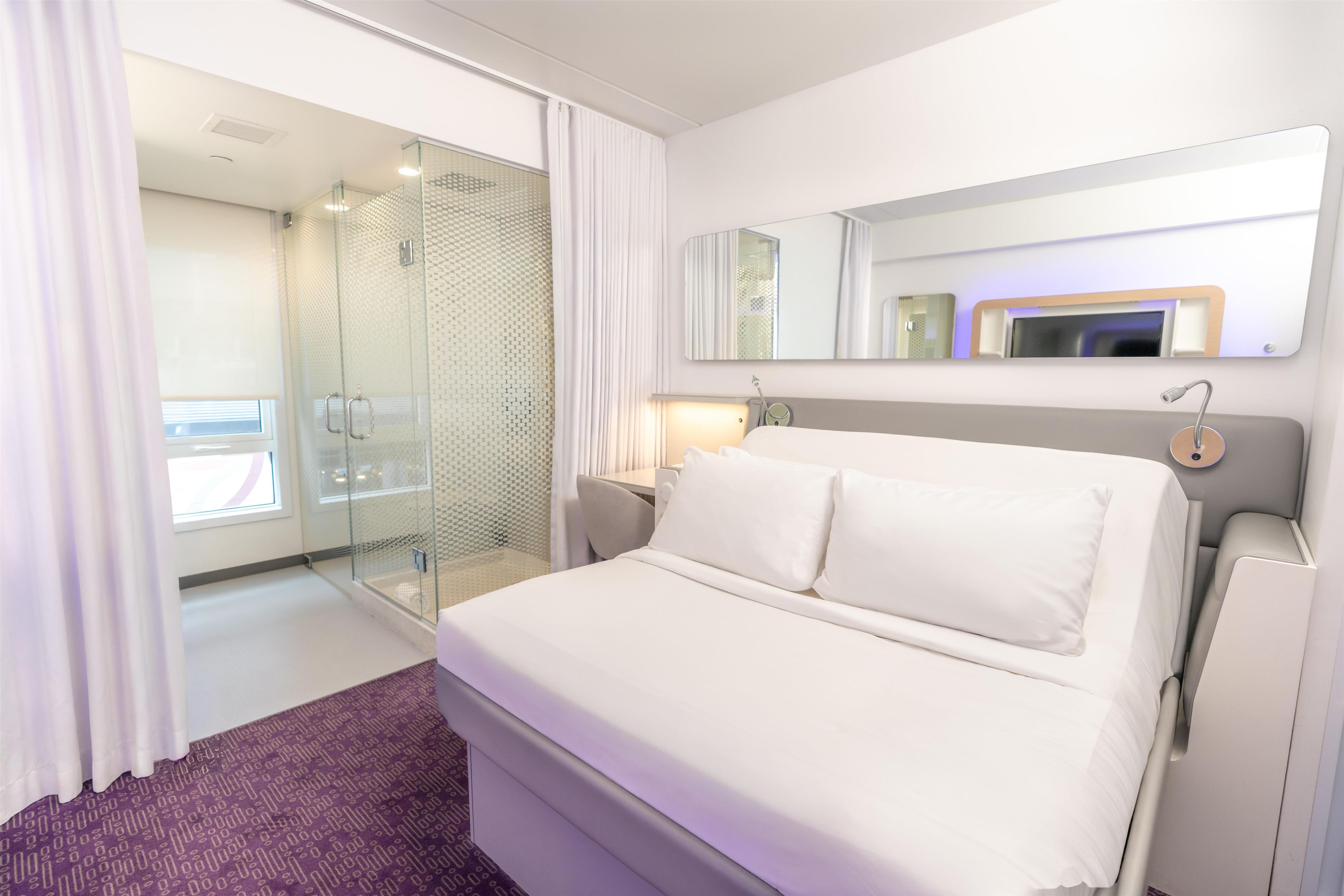 A hotel room with a bed, a shower, a mirror, and a nightstand.
