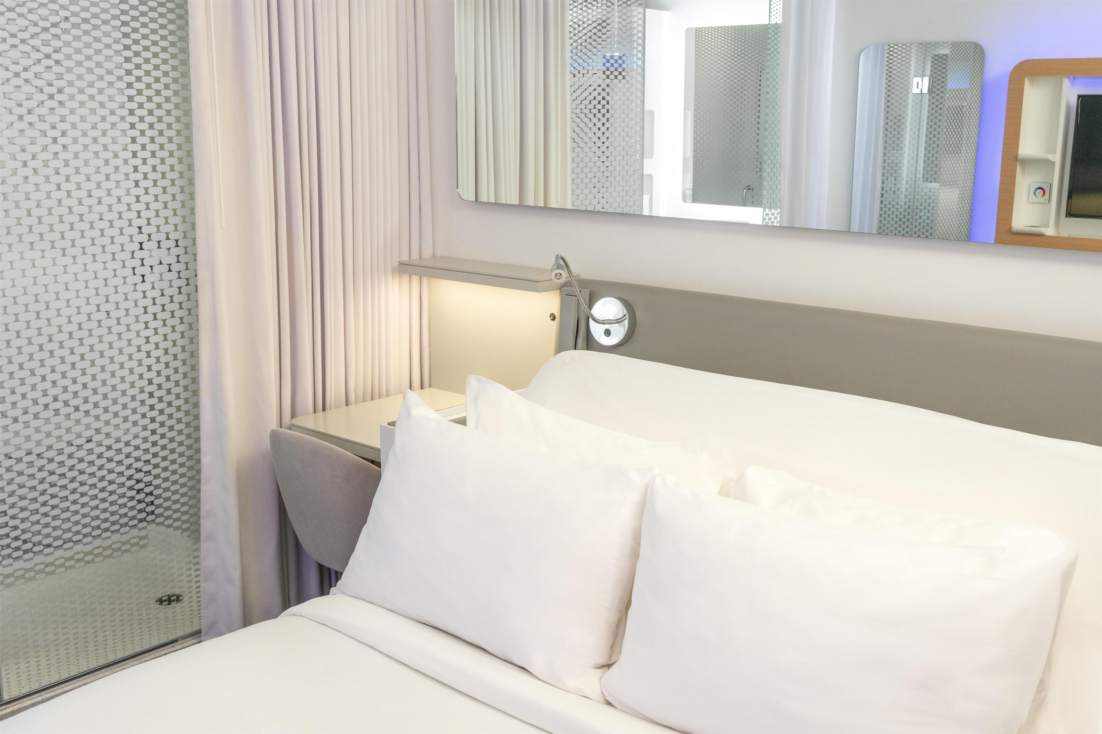A hotel room with a bed, a nightstand, a mirror, and a shower area.