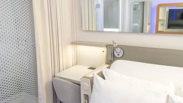 Una habitación de hotel con cama, mesita de noche, espejo y ventana con cortinas.