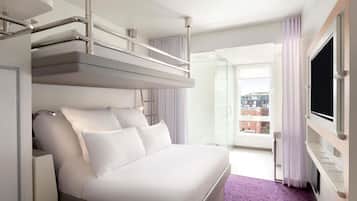 Hotellihuone, jossa on sänky, televisio, parveke ja näkymä kaupunkiin.