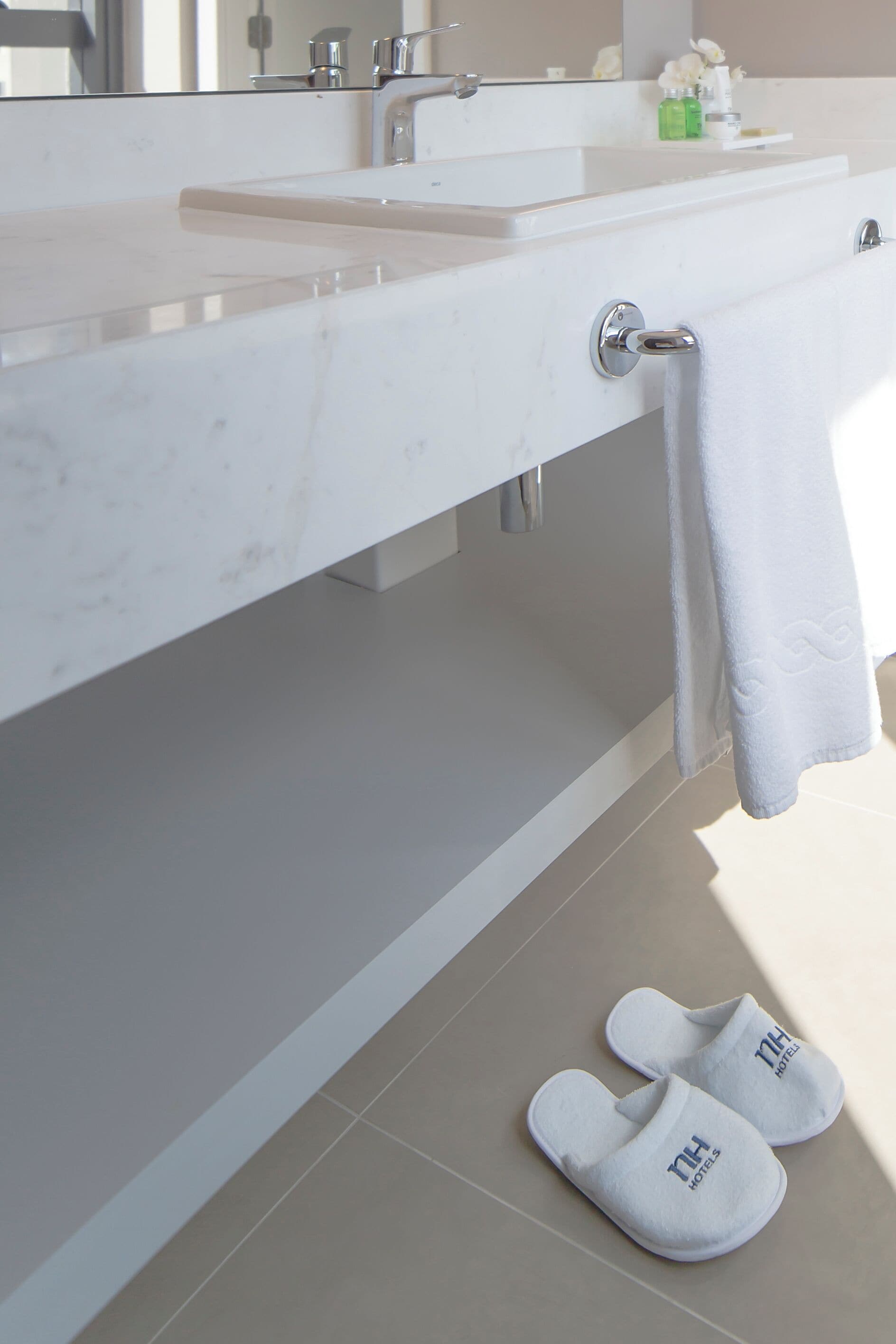 A bathroom with a white sink, a towel hanging on a rack, and a pair of white slippers on the floor.