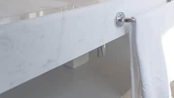 A bathroom with a white sink, a towel hanging on a rack, and a pair of white slippers on the floor.