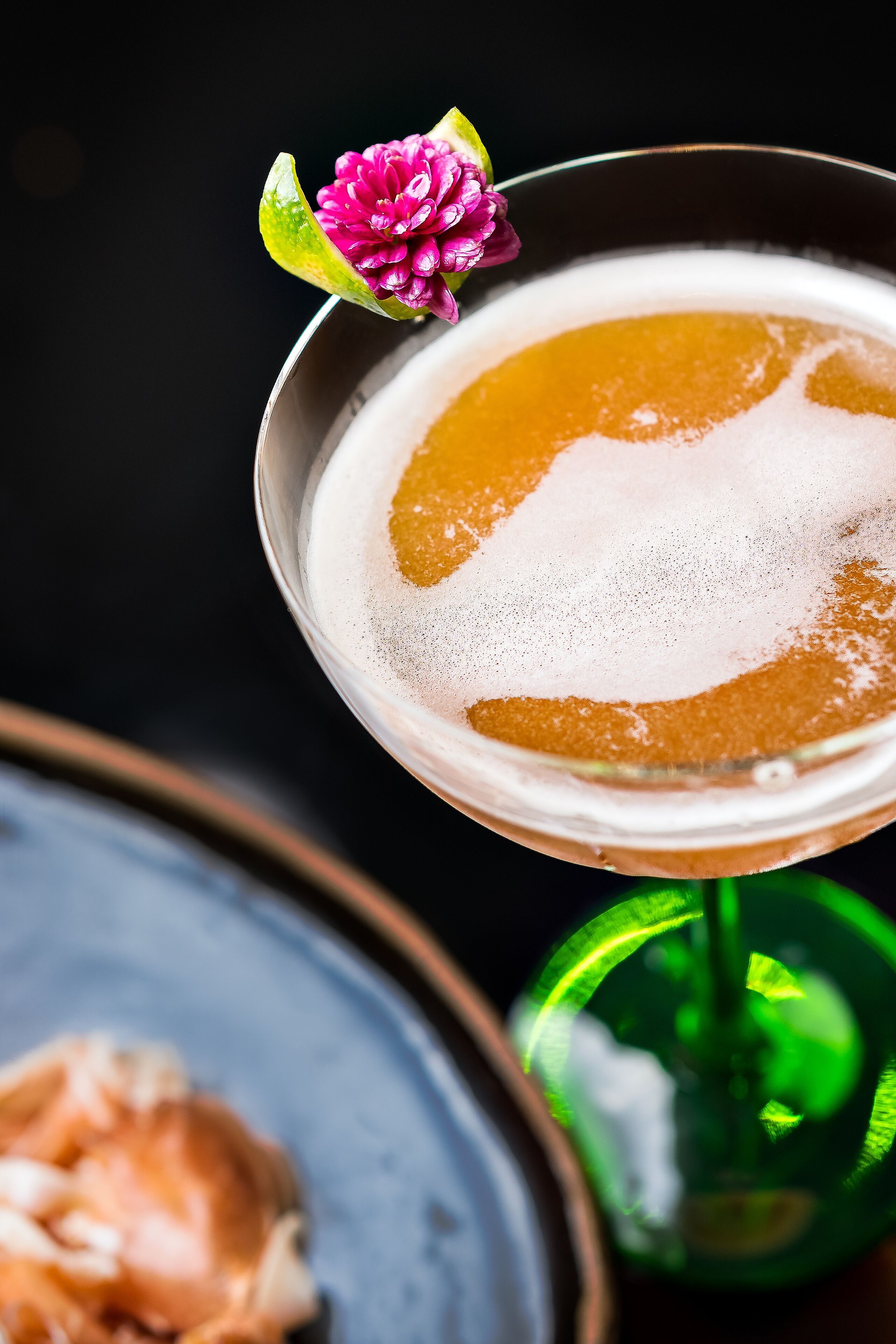 Un cóctel en una copa de martini con una decoración floral, sobre un fondo oscuro.