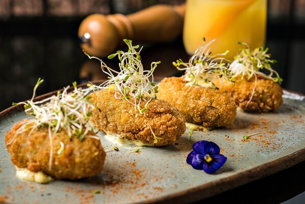 Tres bolas rebozadas adornadas con brotes y una flor azul sobre un plato de cerámica.