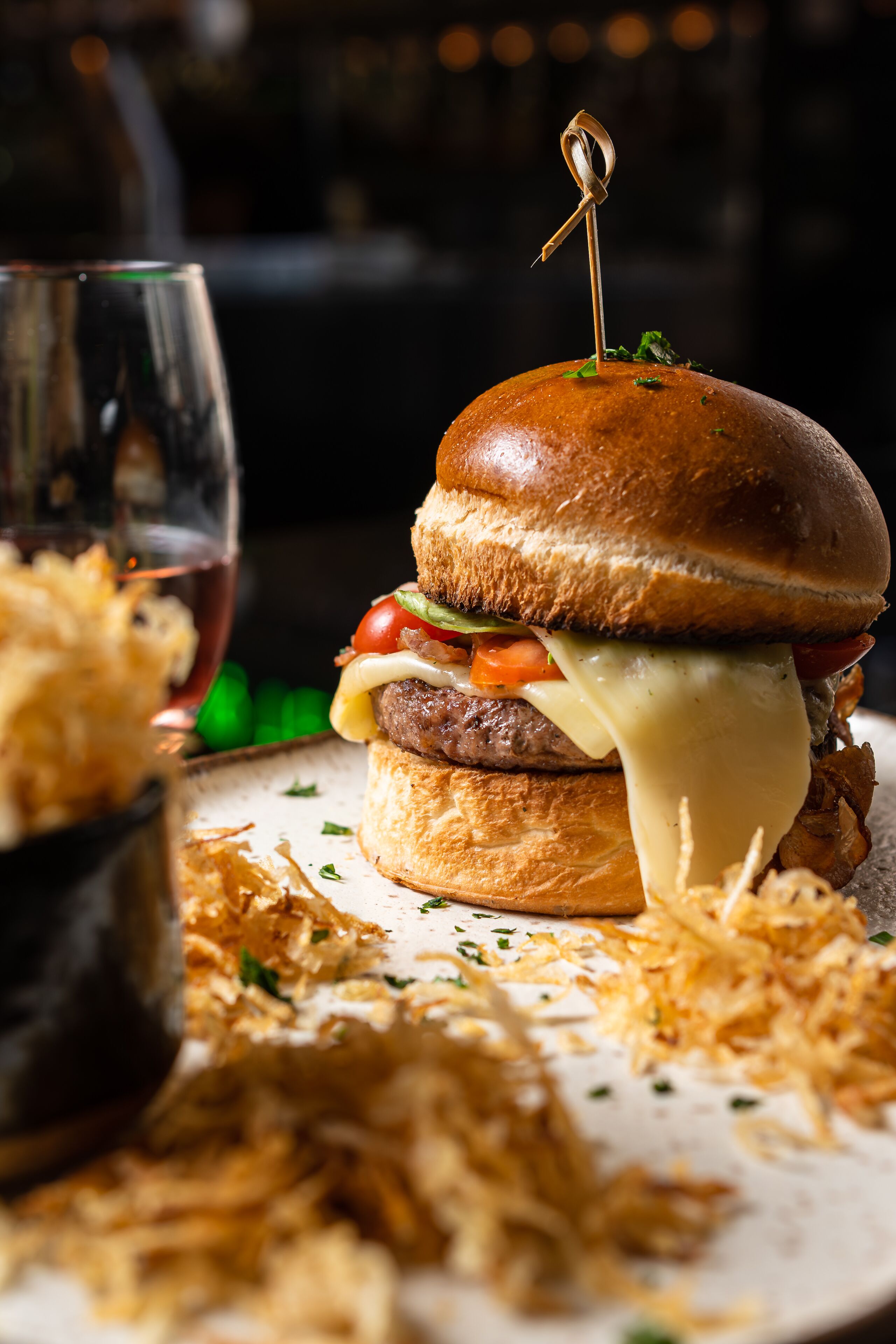 Una hamburguesa con un palillo encima, rodeada de queso rallado y decorada con hierbas.