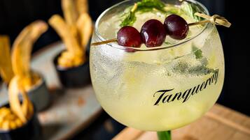 A cocktail glass with a straw, garnished with cherries and mint leaves, labeled "Tangy."