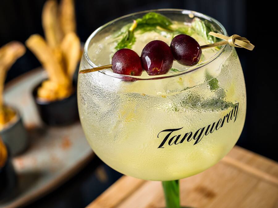 A cocktail glass with a straw, garnished with cherries and mint leaves, labeled "Tangy."