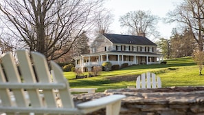 A large house with a porch, surrounded by trees and a grassy hill. - Allenberry Resort (Boiling Springs)