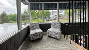 A covered porch with two patterned chairs, a view of a residential area, and a staircase. - Allenberry Resort (Boiling Springs)