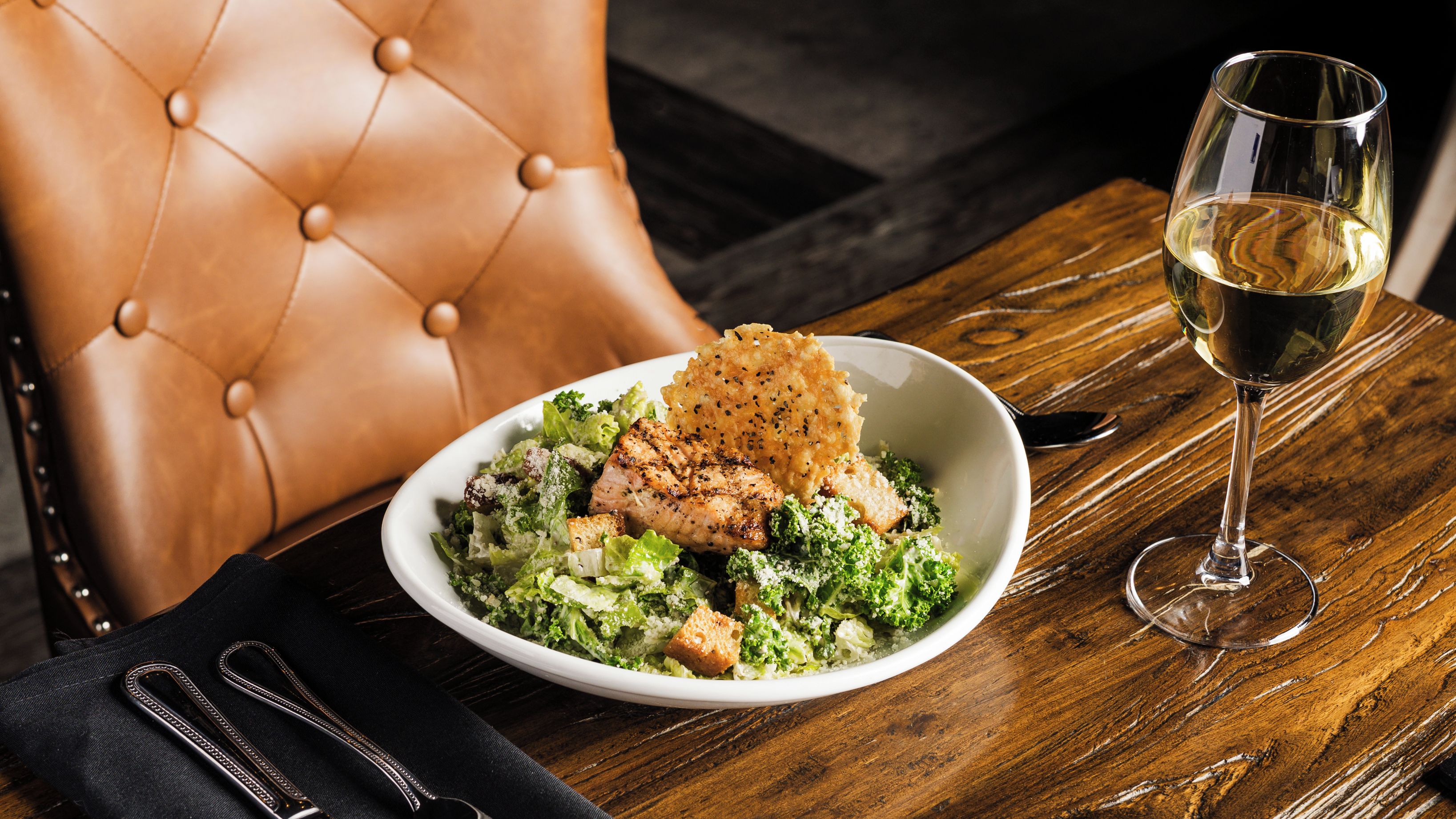 Una mesa de comedor con un plato de comida, una copa de vino y una silla de cuero.
