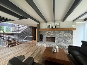 A modern living room with a stone fireplace, wooden staircase, and a black leather sofa. - Allenberry Resort (Boiling Springs)