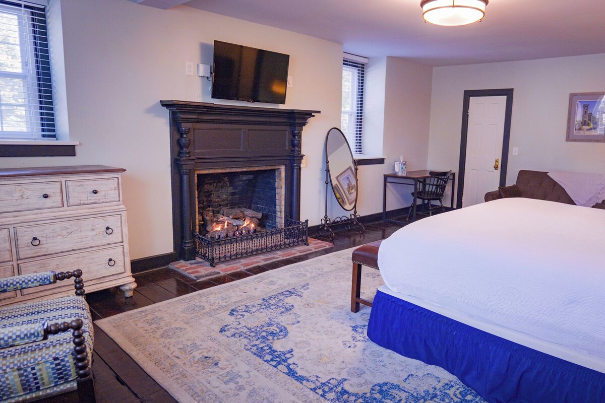 A bedroom with a fireplace, a bed, a dresser, and a chair.