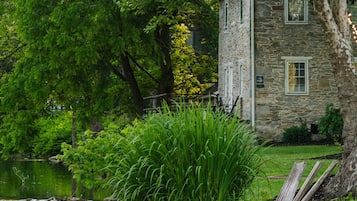A stone house with a pond, surrounded by lush greenery and a wooden bench.