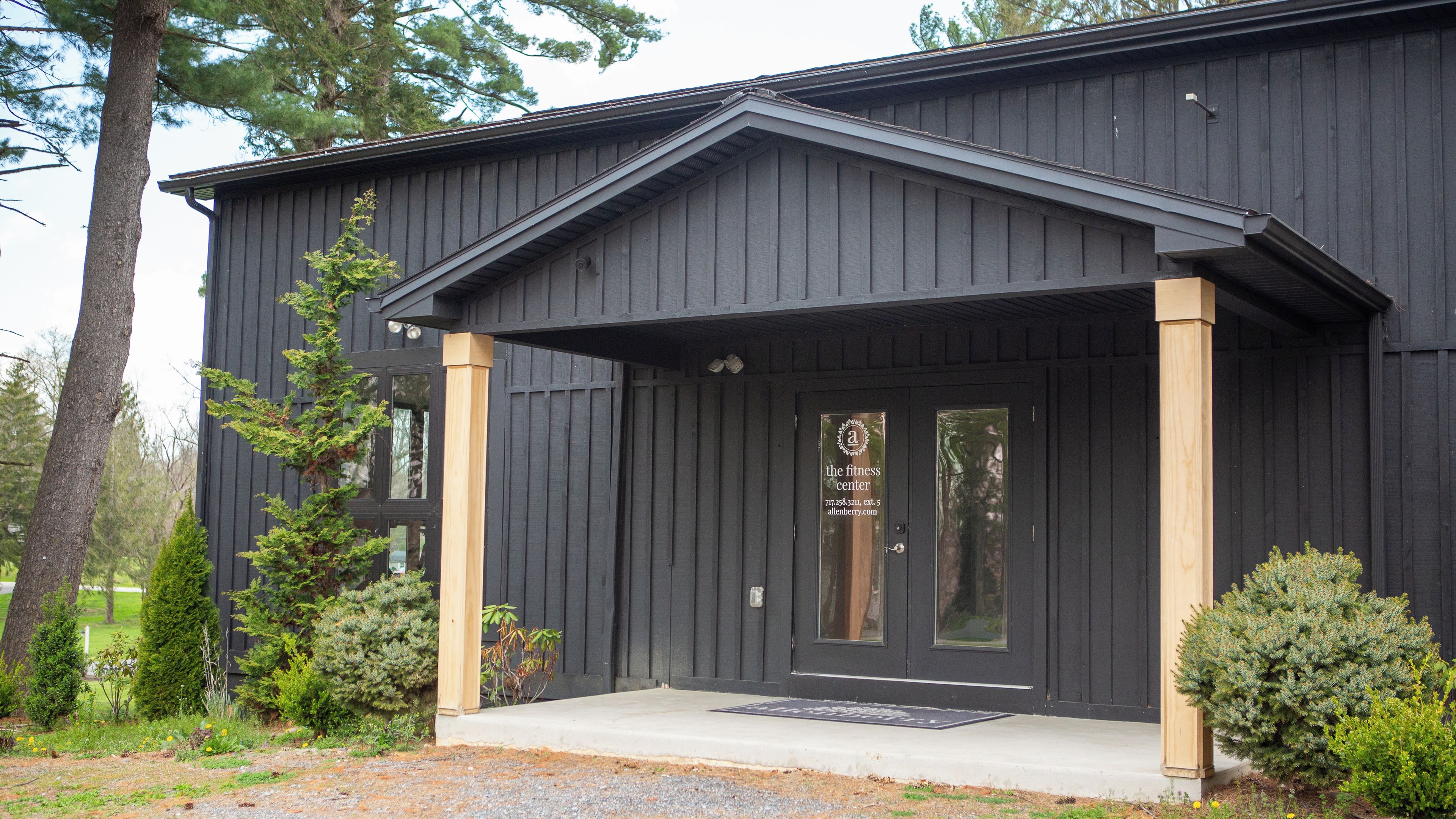 A black building with a front porch, a door with a logo, and a small garden area with shrubs.