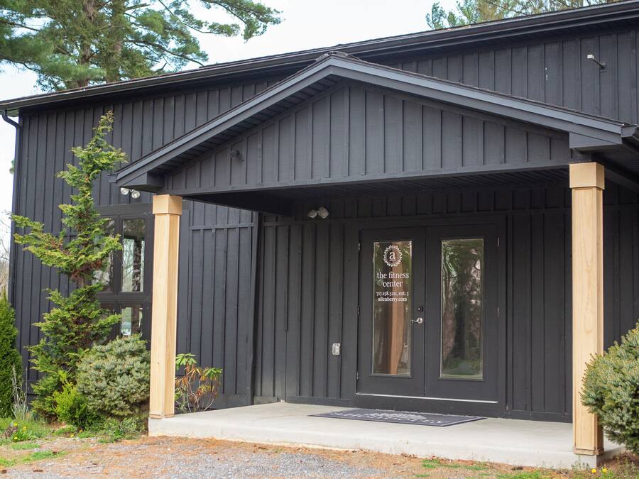 A black building with a front porch, a door with a logo, and a small garden area with shrubs.