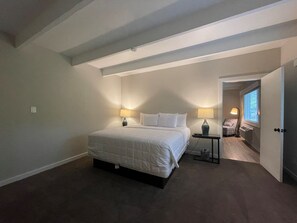 A bedroom with a large bed, two bedside lamps, a small table, and a door leading to another room. - Allenberry Resort (Boiling Springs)