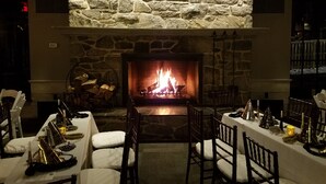 A stone fireplace with a fire, surrounded by tables set for dining, chairs, and a stone wall. - Allenberry Resort (Boiling Springs)